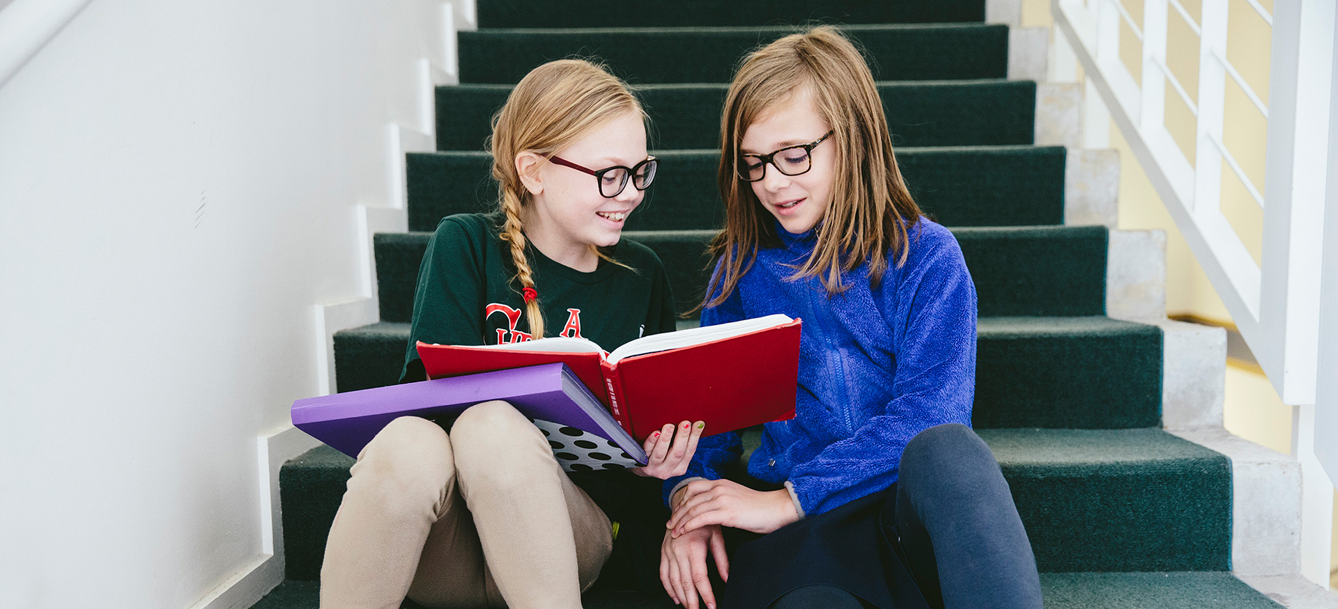 Two students sitting on school stairs reading a book together.